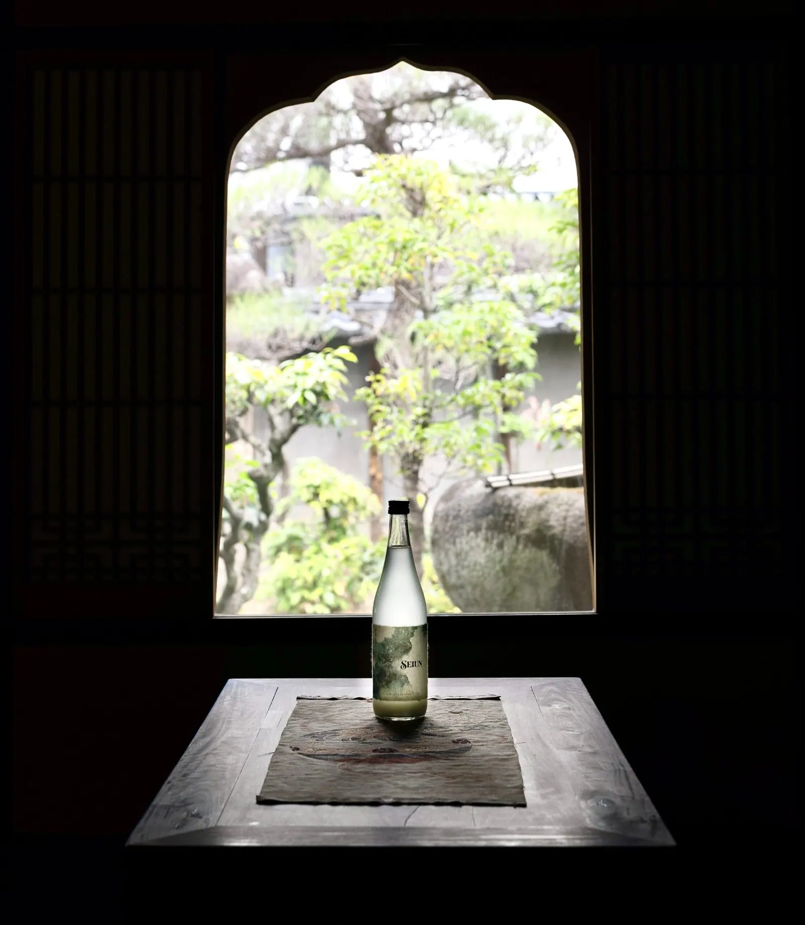 Een fles Seiun op tafel voor een raam met uitzicht op een Japanse tuin